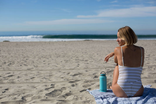 Person sitting on a luxury travel towel on a beach looking out to the ocean